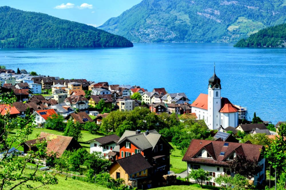 Vista panorámica de Weggis, Suiza, con su iglesia y casas tradicionales junto al lago de Lucerna y rodeado de montañas.