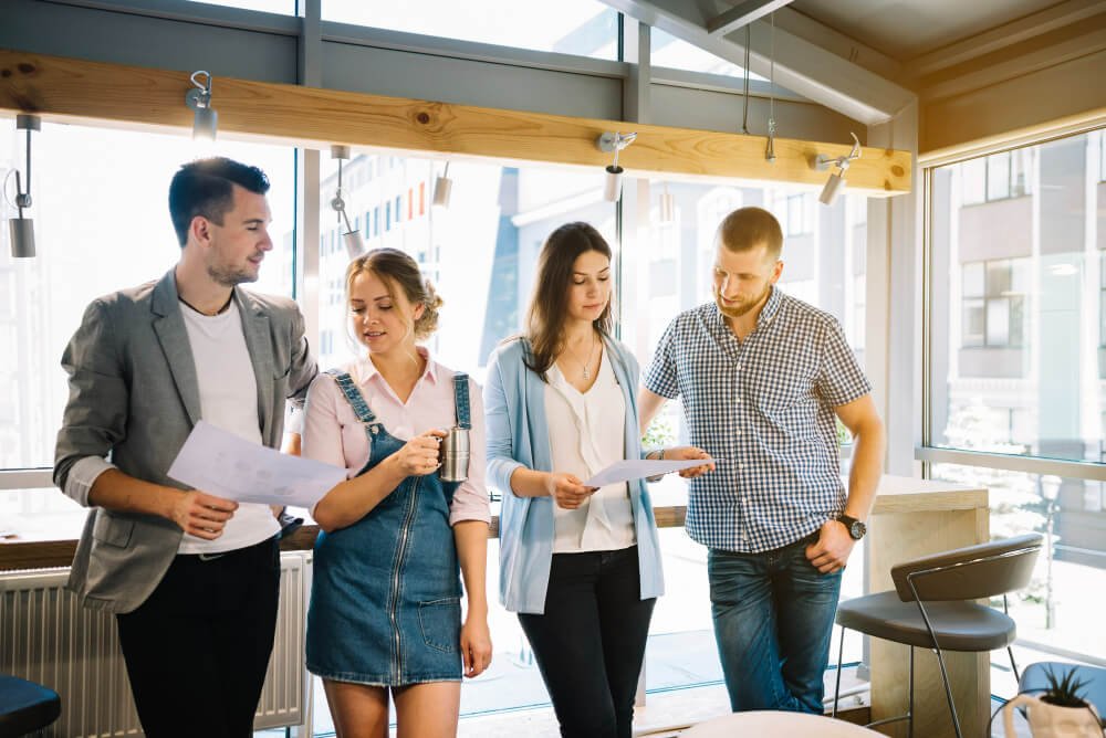 Grupo de jóvenes profesionales en una oficina moderna, discutiendo y revisando documentos en equipo.