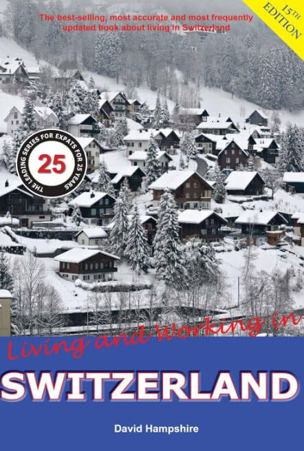 Portada del libro "Living and Working in Switzerland" de David Hampshire, mostrando una aldea suiza nevada rodeada de árboles y casas típicas. Destaca el logotipo de "25 años de guía para expatriados"