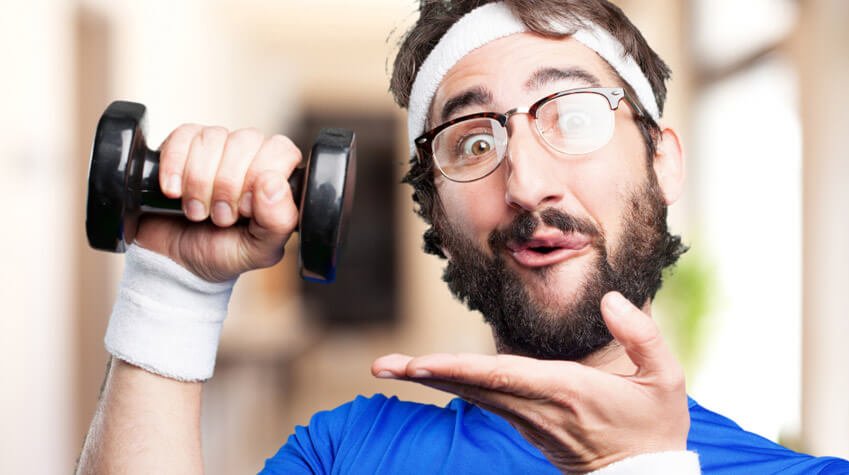 Hombre con gafas y cinta en la cabeza, levantando una pequeña mancuerna negra con una expresión divertida en el rostro. Lleva una camiseta azul y muñequeras blancas, en un ambiente de gimnasio o entrenamiento. _credito a kues1