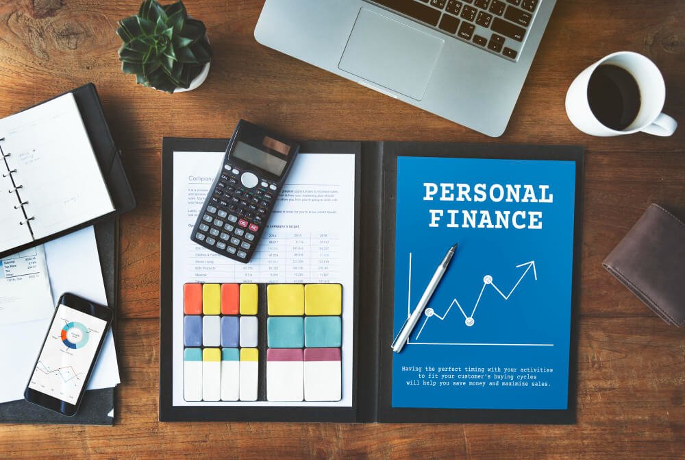 Escritorio con materiales de planificación financiera personal, incluyendo una calculadora, gráficos y un cuaderno titulado 'Personal Finance'