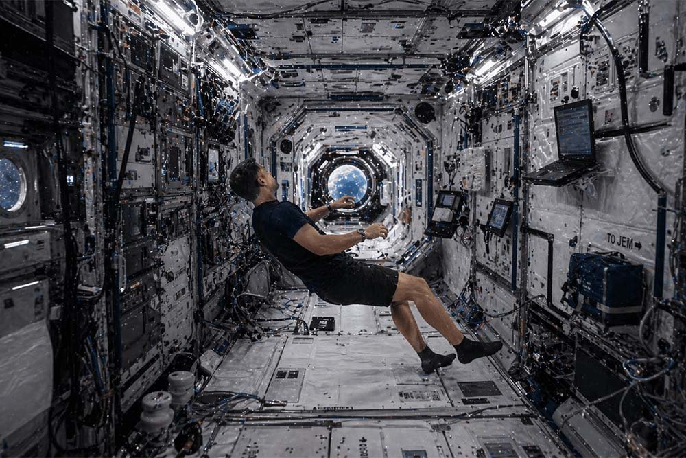 Astronauta flotando en el interior de un módulo espacial en microgravedad, rodeado de equipos y paneles tecnológicos.